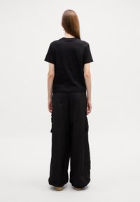 T-shirt en coton noir à manches courtes, associé à un pantalon noir ample avec poches cargo, le tout affichant une texture lisse.