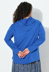 Felpa con cappuccio blu a maniche lunghe, realizzata in tessuto morbido, con una vestibilità comoda e un orlo curvo. Caratterizzata da cappuccio con coulisse e polsini a contrasto.