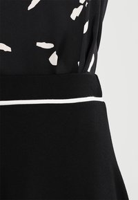 Svart klänning med ett vitt abstrakt mönster på ett lättviktigt tyg, med en kontrasterande svart midja med en vit kantdetalj.