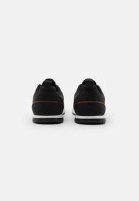 Zwarte sneakers met een gestructureerde mesh bovenkant, een gladde rubberen zool en contrasterende bruine accenten. Voorzien van trekflappen voor eenvoudig aan- en uittrekken.