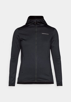 Svart zip-up jakke med en tettsittende design, lett materiale, høy krage, lange ermer, og en logo på brystet. Myk tekstur, minimal aksent.