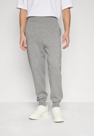 Szürke, puha pamut keverékből készült melegítőnadrág, rugalmas derékkal, szűkített bokákkal és oldalsó zsebekkel, fehér sportcipővel párosítva.