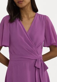 Fialová zavinovací šaty s krátkými, volánkovými rukávy, V-výstřihem a zavázáním v pase. Vyrobeno z hladké, lehké tkaniny.