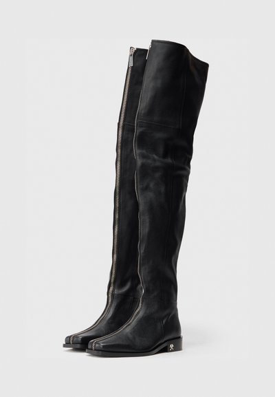 Botas de cuero negras hasta la rodilla con un diseño elegante, que cuentan con un cierre de cremallera en la parte delantera y un tacón plano y brillante con detalle de acento.