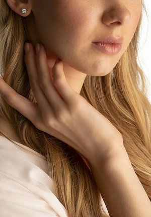 Silberne Stud-Ohrringe mit floralem Design, verziert mit kleinen, klaren Edelsteinen, getragen von einer Person mit langen, welligen blonden Haaren.