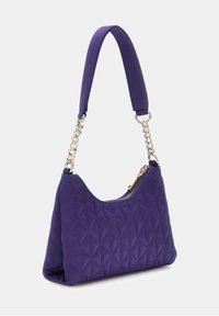 Sac à main en velours violet avec une forme courbée, doté d'une bandoulière rembourrée et d'accents en chaîne dorée, complété par une fermeture zippée.