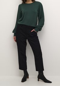 Pull vert à manches longues avec des épaules côtelées, associé à un pantalon noir taille haute et des bottines noires à talon aigu.