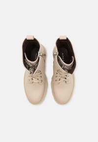 Botines beige de cuero con textura suave. Presentan ojales, cierre con cordones y un adorno de cremallera decorativa en el lateral.