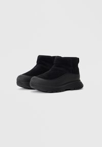 Botas de tornozelo pretas feitas de camurça com uma sola de borracha texturizada. Apresentam um design simples, sem hardware ou adornos visíveis.