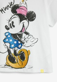Hvid bomuld t-shirt med et farverigt grafik af en tegneseriemus, der bærer en blå prikket kjole og gule sko.