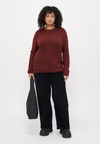 Pulover tricotat de culoare vișinie, cu o croială lejeră și un model texturat; asortat cu pantaloni din catifea lățită negri și pantofi cu platformă grosieră negri. Geantă neagră tip tote.