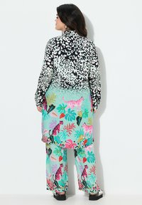 Outfit multicolore con una maglietta leopardata bianca e nera e pantaloni verde menta con motivi di foglie tropicali e tigri.