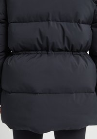 Chaqueta puffer negra hecha de un material ligero, con secciones acolchadas y una cinturilla elástica, que presenta una textura suave y mate.