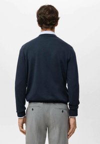 Marineblauw poloshirt met lange mouwen van gebreide stof, voorzien van een kraag en geribbelde manchetten, gedragen met lichtgrijze maatbroek.