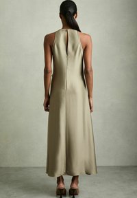 Abito lungo senza maniche di un colore oliva tenue, realizzato in un tessuto liscio. Presenta un'apertura a chiave sul retro e una vestibilità ampia con design minimale.