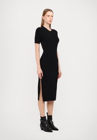 Black knitted dress featuring short sleeves, a fitted silhouette, diamond pattern, and side slits. Worn with black ankle boots.