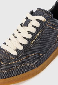 Tenis em denim com atacadores creme, logótipo em relevo dourado, costura em tom contraste e sola de borracha de goma. Apresenta um design de perfil baixo.