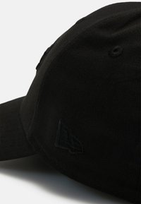 Juodas beisbolo kepurė iš tekstūruotos medžiagos, su šiek tiek išlenktu rėmeliu ir siuvinėjimu tamsesniu atspalviu šone.