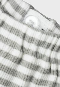 Tessuto di cotone a righe in grigio e bianco, con chiusura a bottone e costine testurizzate lungo la vita. Vista ravvicinata mostra i dettagli.