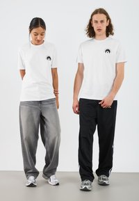 Hvite t-skjorter med et lite grafikk på brystet, grå baggy jeans og svarte joggebukser, kombinert med sølvfargede sneakers.