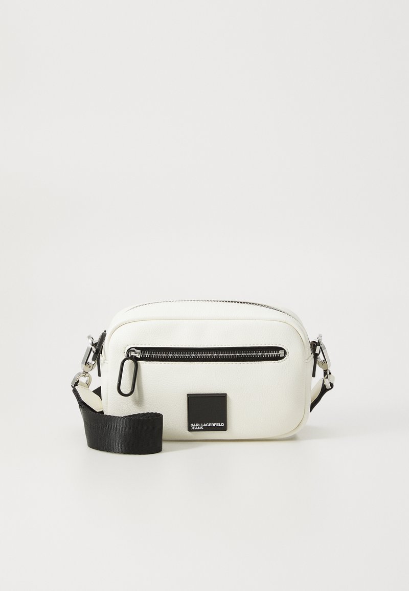 White leather crossbody bag with a zippered main compartment, black strap, and a rectangular logo patch on the front. Smooth texture.