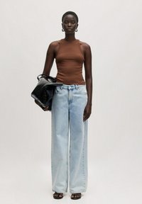 Bruine mouwloze top, lichtblauwe wijde jeans, zwarte handtas, platte zwarte sandalen. Soepele texturen en een getailleerde pasvorm.