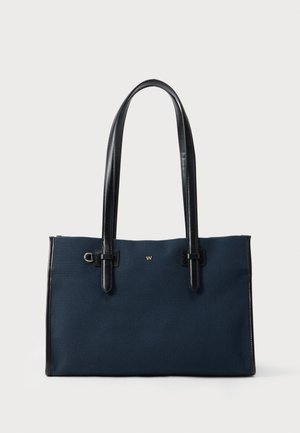 Sac cabas rectangulaire bleu marine avec poignées et bordures en cuir noir, petit emblème doré en forme de "W" et détail en anneau doré près du coin supérieur gauche.