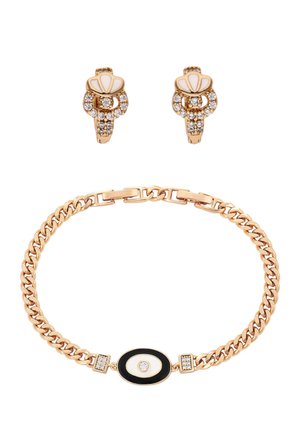 Kultainen rannekoru, jossa on mustavalkoinen soikea keskiosa, ja siihen sopivat kultaiset korvakorut, joissa on valkoista emalia ja kirkkaita kristalleja.