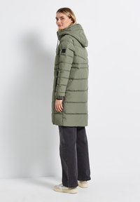 Groene pufferjas met een capuchon, horizontaal gestikt ontwerp, ribgebreide manchetten, twee zijritsen en een labeldetail op de linkerschouder.