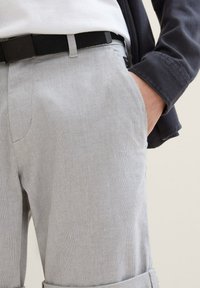 Pantalones de textura gris claro con un corte relajado, que cuentan con bolsillos frontales, un cinturón de tejido negro y un detalle de puño en el dobladillo.