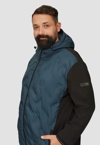 Czarna i turkusowa kurtka puchowa z kapturem, z zapięciem na zamek, bocznymi kieszeniami i teksturowanym materiałem. Naszywka z logo na lewym rękawie.
