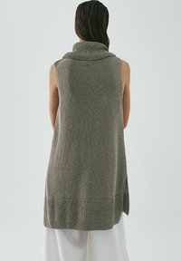 Gilet lungo senza maniche in maglia grigia con colletto alto, orlo a costine, fessure laterali e una finitura testurizzata. Corpo in maglia liscia contro accenti a costine.
