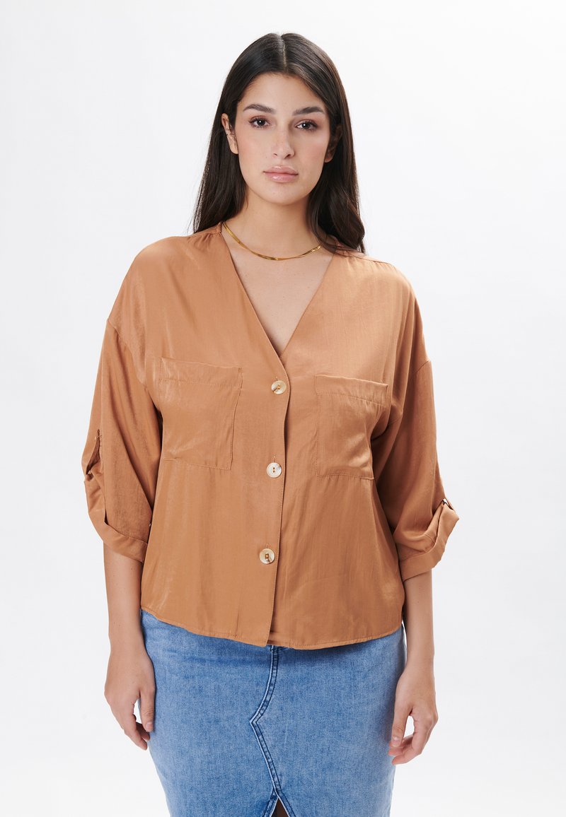 Blusa in raso color ruggine con scollatura a V, bottoni e due tasche frontali. Presenta maniche leggermente arrotolate e una vestibilità ampia.