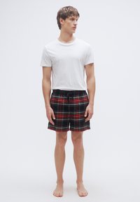 Μαύρα και κόκκινα καρό σορτς με ελαστική μέση και κορδόνι, σε συνδυασμό με λευκό μονόχρωμο t-shirt. Το μοντέλο στέκεται ξυπόλητο, με τα χέρια στο πλάι.