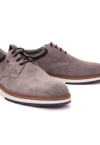 Chaussures en daim gris à lacets avec un bout arrondi, des accents en cuir et une semelle intermédiaire blanche arborant une semelle extérieure en caoutchouc marron.