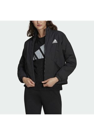 Black lightweight jacket with a zip closure, elastic cuffs, and a small white logo on the chest. Worn over a black patterned shirt.