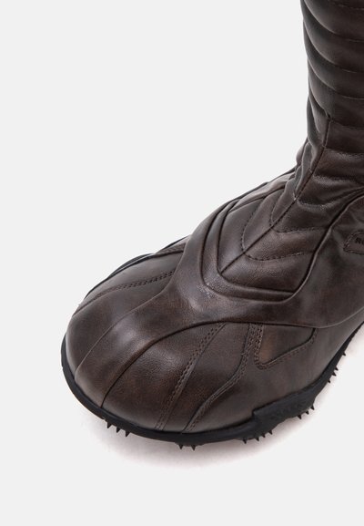 Gros plan d'une botte en cuir marron foncé avec des coutures détaillées et une semelle noire avec des crampons en caoutchouc.