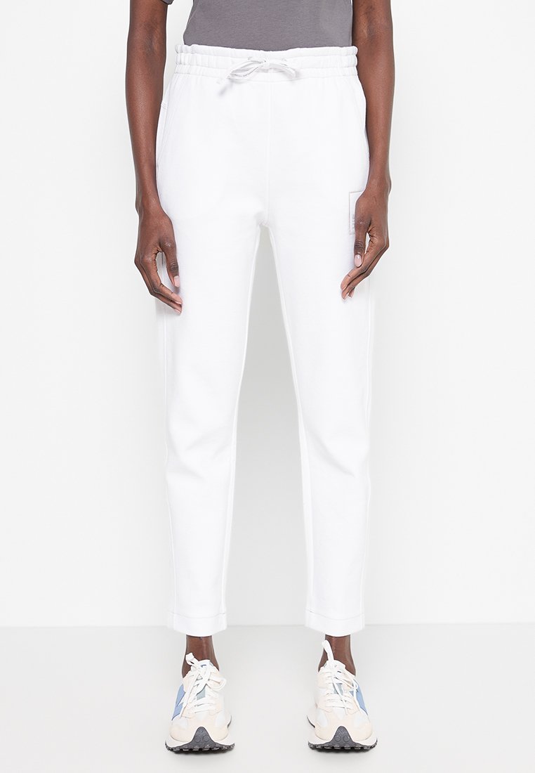 Weiße Jogginghose mit elastischem Bund und Kordelzug, ausgestattet mit einer Seitentasche. Kombiniert mit hellen Sneakers.