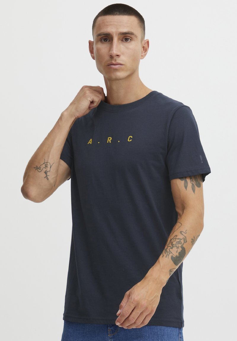Tamsiai mėlynos spalvos medvilnės T-shirt, su apvaliu kaklu, trumpomis rankovėmis, ant priekio yra geltonos spalvos užrašas "A.R.C.". Paprastas dizainas su laisvu kirpimu.