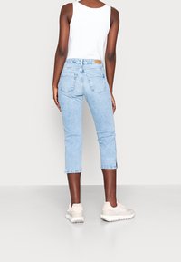 Vaaleansiniset farkut, joissa on lyhennetty malli, suora lahje, takataskut ja huomaamattomat tikkausdetailit. Yhdistetty vaaleisiin lenkkareihin.