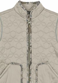 Veste matelassée beige avec col montant, fermeture éclair à l'avant et deux poches latérales. Doublure intérieure présentant un motif coloré d'animaux.