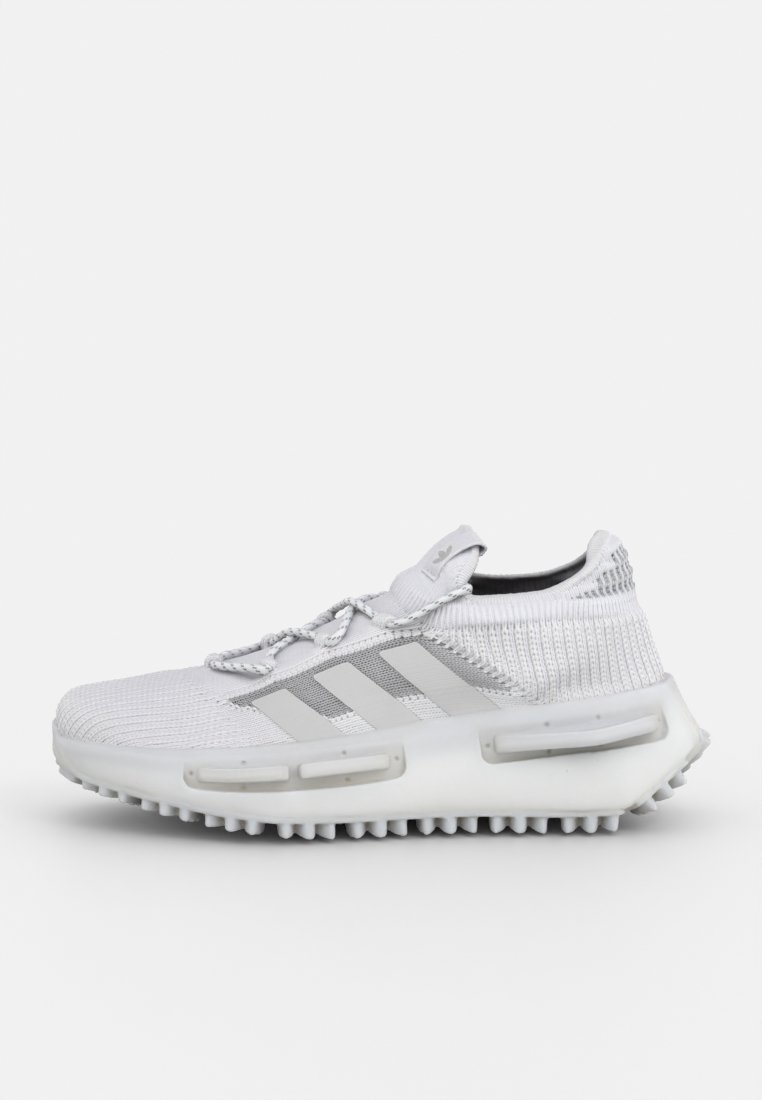 Sneaker bianca con tomaia in maglia, dettagli argentati testurizzati e tre strisce grigie. Presenta una suola spessa e imbottita con grip.