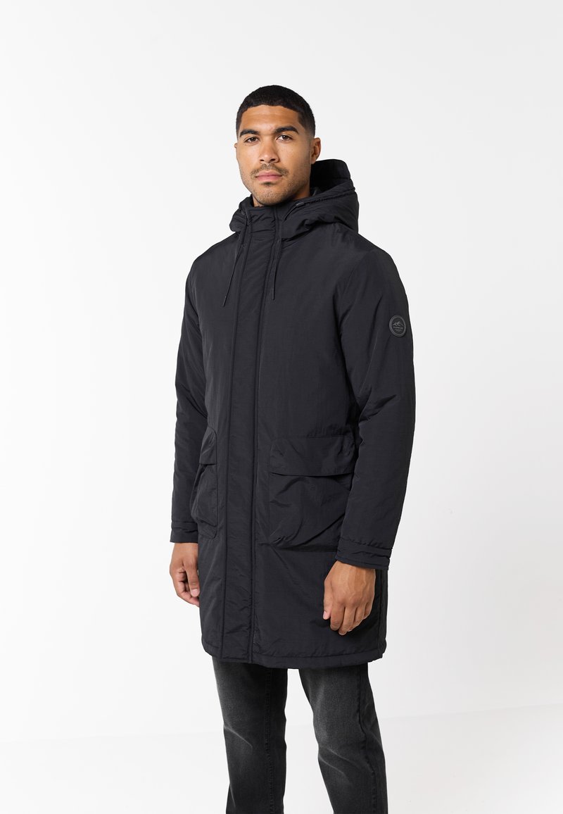 Parka nera con cappuccio, caratterizzata da una zip frontale, due grandi tasche anteriori e polsini elasticizzati, con una texture liscia e opaca.