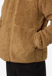 Rjava jopa iz fleec materiala z teksturirano, puhasto površino, z zadrgo spredaj in stranskimi žepi. poudarki v svetlo rjavi obrobi.