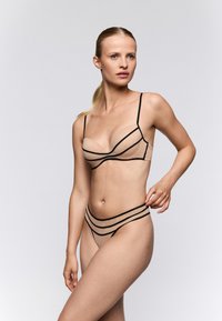 Naaktkleurige lingerie set met zwarte bies, bestaande uit een gevormde beha met dunne bandjes en een bijpassende bikinibroek met gelaagde strepen.