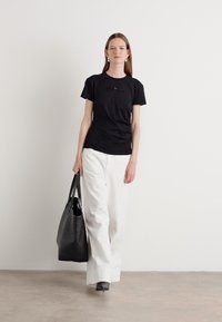 Maglietta nera a maniche corte con un design testurizzato, abbinata a pantaloni bianchi a vita alta e una grande borsa a tracolla nera.