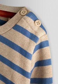 Pulover bej cu dungi orizontale albastre. Prezintă guler rotund și doi nasturi bej pe umăr. Textură moale tricotată.
