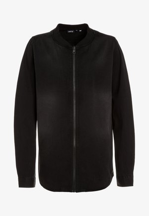 Veste noire à manches longues zippée, col rond et sans poches visibles, présentée sur un fond blanc uni.