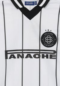 Biała koszulka piłkarska z czarnymi pionowymi paskami, czarnym kołnierzem w kształcie V oraz logo "PANACHE" i "ONLY & SONS CLUB MUNDIAL."