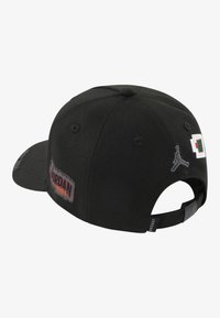 Svart caps laget av stoff med buet skjerm. Har broderte detaljer, inkludert et Jumpman-logo og en "Jordan 1984"-lapp. Justerbar bak.